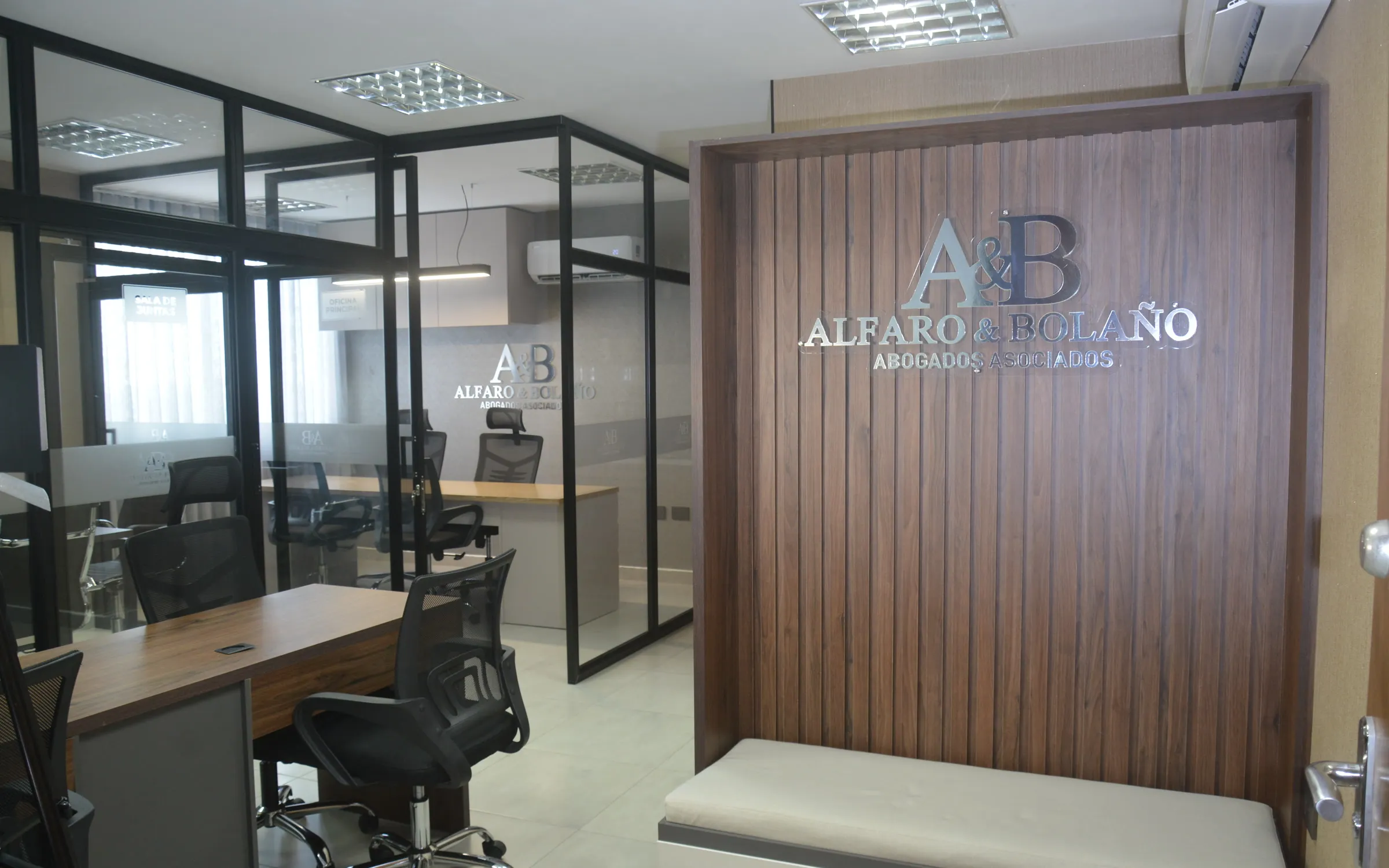 Recepción de Alfaro y Bolaño con muro de madera, logo institucional y oficinas en vidrio